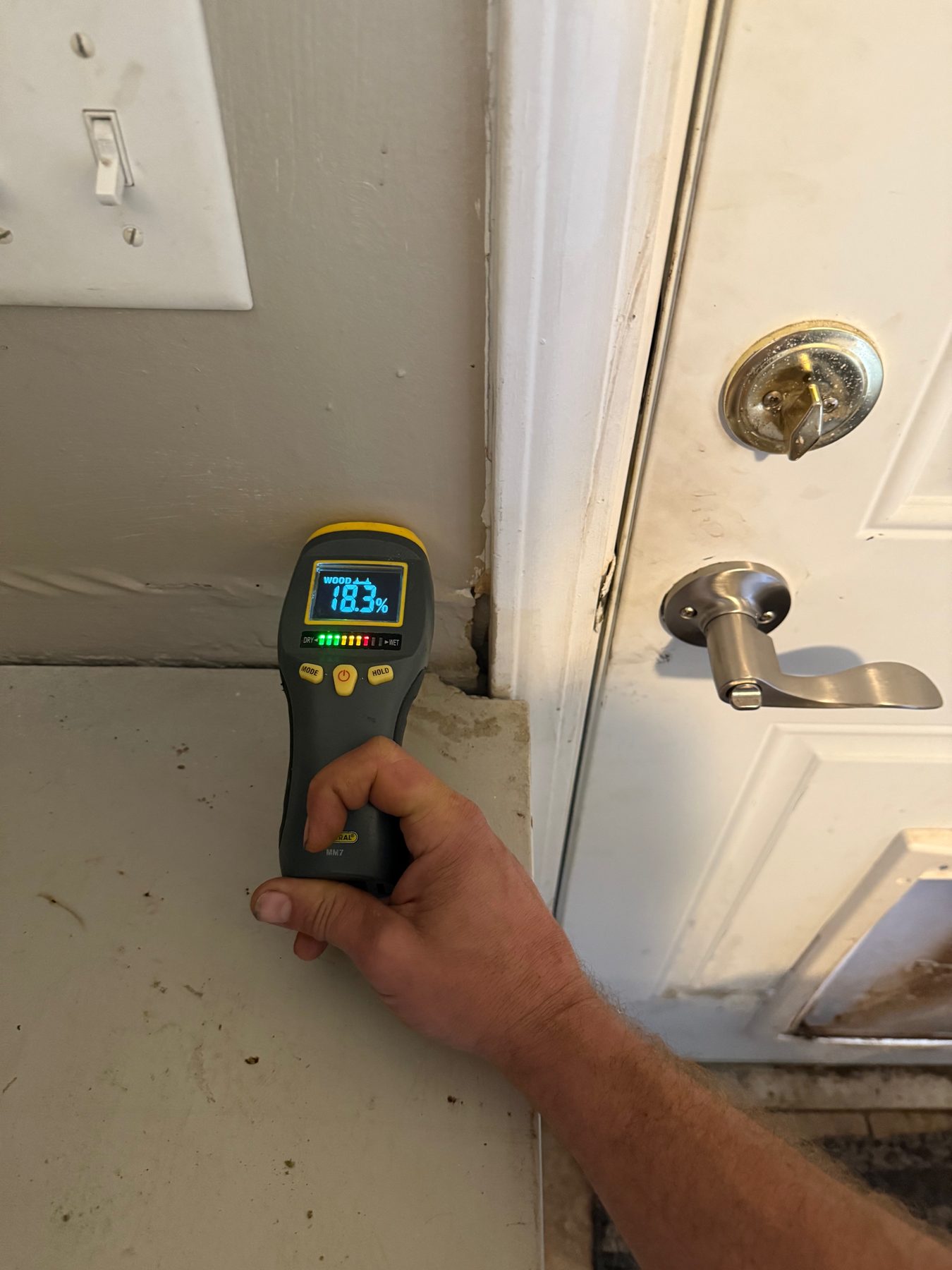 A moisture meter reading 18.3 percent at a door frame